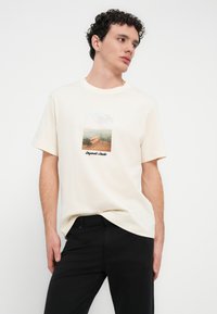 Κρεμ T-shirt από βαμβάκι, με τυπωμένη εικόνα ενός λιμανιού με νερό. Μανίκια κοντά, στρογγυλή λαιμόκοψη, άνετη εφαρμογή.