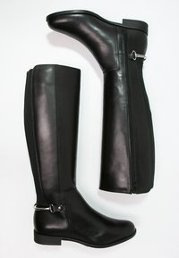 Bottes noires jusqu'aux genoux en cuir lisse, avec une fermeture éclair sur le côté, un panneau en tissu contrastant et un accent de boucle en argent au talon.