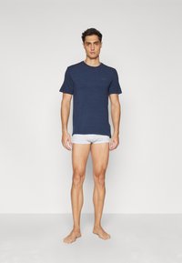 T-shirt de manga curta azul marinho em um tecido suave com um logo discreto. Combinado com boxers cinza claro, exibido contra um fundo simples.