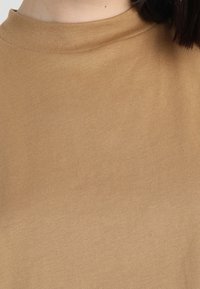 Camiseta de algodón marrón con cuello redondo y mangas cortas, que presenta una textura suave y un diseño liso. Sin patrones ni logotipos visibles.