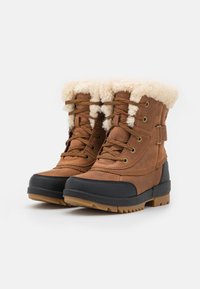 Botas impermeables marrones con un forro de piel de imitación color beige, cordones en la parte frontal, capuchón de goma en la puntera y suela texturizada para mayor agarre. Acentuadas con ojales de metal.