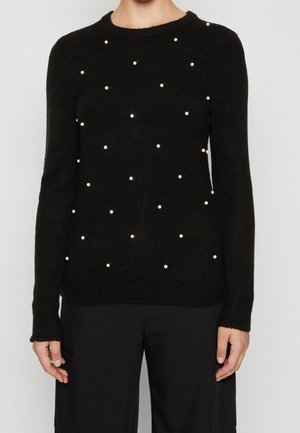 Pull noir en matériau doux, avec un col rond et décoré de perles blanches éparpillées sur le devant. Manches longues.