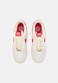 Sneaker Nike Air Force 1 bianchi e beige con accenti e lacci rossi. Punta perforata, colletto imbottito e soletta con motivo floreale.