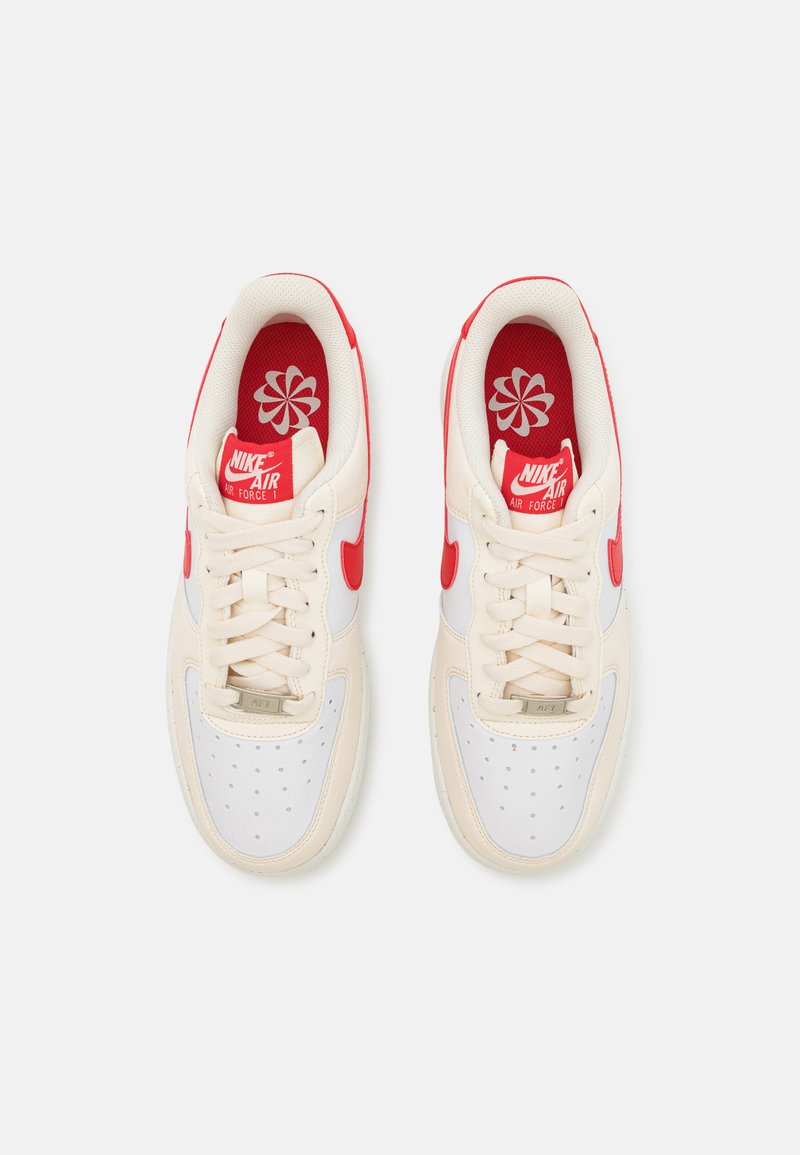 Weiße und cremefarbene Nike Air Force 1 Sneaker mit roten Akzenten und Schnürsenkeln. Perforierte Zehenbox, gepolsterter Kragen und floral gemusterte Innensohlen.