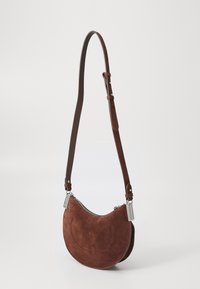 Hnědá kabelka z broušené usně se zakřiveným tvarem, nastavitelným koženým popruhem, stříbrnými kovovými prvky a zipovým uzávěrem. Hladká textura s prošitými detaily.