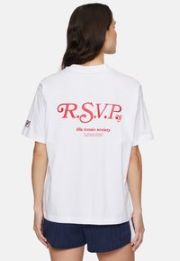 Valkoinen puuvillapaita, jossa on punainen "R.S.V.P." ja "fila tennis society" -teksti selässä. Rentomallinen, lyhythihainen ja pyöreäkauluksinen.