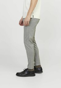 Pantaloni grigi a gamba affusolata realizzati in un tessuto morbido e con una texture, abbinati a scarpe nere con lacci e calze scure, mostrati di lato.