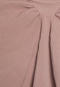 Vêtement en tissu à côtes de couleur rose doux, avec des fronces au niveau du buste, présentant une texture lisse et un design fluide.