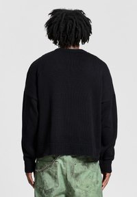 Maglione nero a maglia con spalle abbassate, polsi a costine e orlo corto. Il motivo testurizzato aggiunge profondità al tessuto.