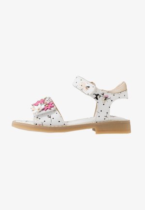 Białe sandały z kwiatowymi zdobieniami, kropkami i rzepem. Posiadają płaską, brązową podeszwę oraz ozdobne przeszycia.