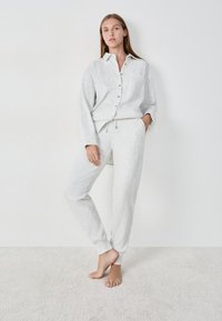 Lichtgrijze, geribbelde loungewear-set met een knoopsluiting-shirt met een zak en broek met trekkoord, beide met elastische boorden. Zachte stof textuur.