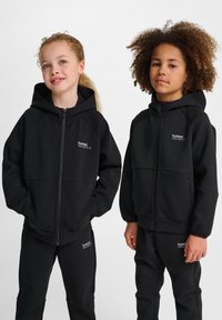 Svarta zip-up huvtröjor med en slät textur, med raglanärmar och logotypdetaljer. Kommer med matchande svarta byxor.