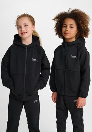 Zwarte zip-up hoodie met een gladde textuur, voorzien van raglanmouwen en logo-accenten. Vergezeld van bijpassende zwarte broek.