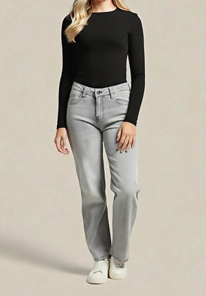 Woman wearing a black long-sleeve top, light gray straight-leg jeans, and white slip-on shoes standing against a plain background.