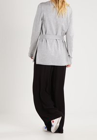 Cardigan grigio a maniche lunghe con cintura a fiocco, abbinato a pantaloni neri larghi e sneakers bianche con dettagli a stelle rosse e blu.