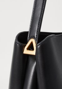 Black leather handbag featuring a triangular gold hardware detail on the strap, smooth texture with a slightly glossy finish.