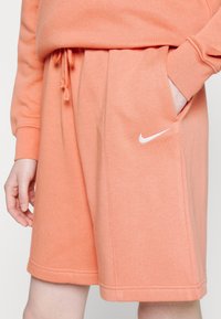 Light orange cotton shorts with an elastic waistband, side pockets, and a white Nike logo on the left leg. Smooth texture, casual fit.