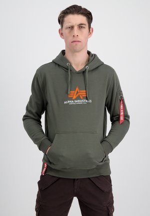 Sudadera verde oliva con bolsillo frontal, capucha con cordón y logo naranja. Presenta una etiqueta roja en la manga, puños y dobladillo acanalados.