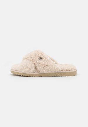 Sandales slide beiges à texture pelucheuse, avec une large lanière croisée et une semelle plate beige. Dotées d'un petit logo métallique.