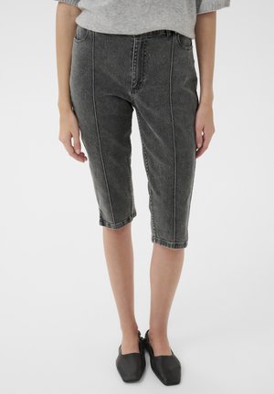 Stredne dlhé tmavosivé džínsové šortky s prednými vertikálnymi švami, nosené so sivým sveterom a čiernymi plochými topánkami so štvorcovou špičkou.