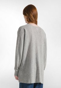 Grauer Langarm-Pullover mit weicher Textur, weitem Rundhalsausschnitt und einem kleinen Markentag auf der Rückseite. Lockerer Schnitt, hinten etwas länger.