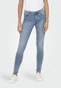 Úzké džíny vyrobené z světle modrého denimu, s polovičním pasem, pěti kapsami a mírně vybledlým vzhledem. Nosené s bílými teniskami.