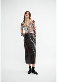 Tricou cu mânecă lungă, cu un model în nuanțe de bej, maro și portocaliu; asociat cu o fustă midi neagră din piele ecologică, cu talie înaltă. Pantofi plate negri și sosete negre.