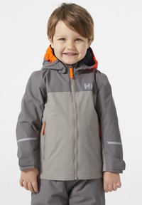 Chaqueta impermeable gris con acentos naranjas, bolsillos con cremallera y tiras reflectantes. Cuenta con capucha y cremallera frontal para facilitar su uso.