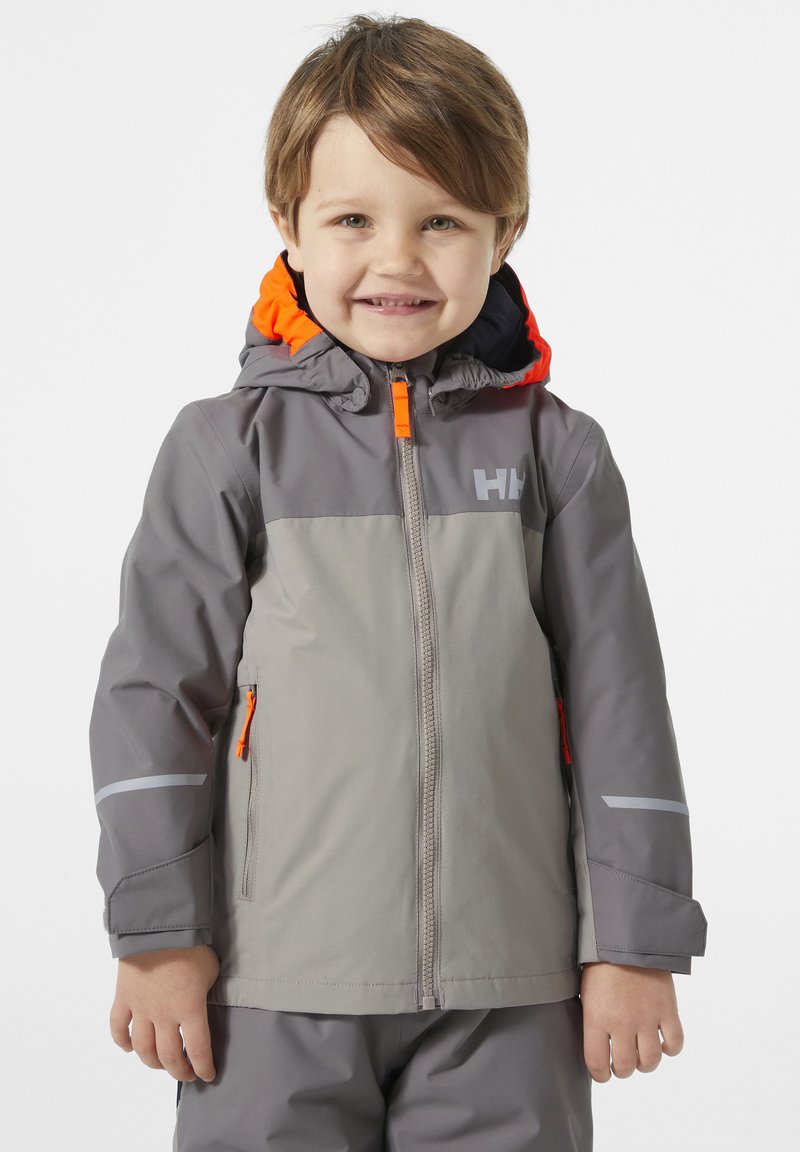 Chaqueta impermeable gris con acentos naranjas, bolsillos con cremallera y tiras reflectantes. Cuenta con capucha y cremallera frontal para facilitar su uso.