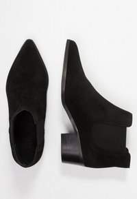 Schwarze Wildleder-Stiefeletten mit einer spitzen Zehenpartie, elastischen Seitenteilen und einem niedrigen Blockabsatz, die eine glatte Textur und ein minimalistisches Design aufweisen.