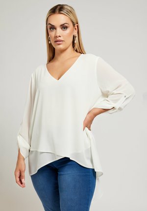 Witte, luchtige blouse met een V-hals en lange mouwen. Heeft een gelaagde zoom en knoopdetails op de mouwen, gemaakt van licht materiaal.