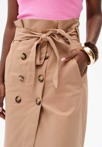 Jupe brune taille haute avec une ceinture �à nouer, comportant de gros boutons et des poches latérales, fabriquée dans un tissu texturé.
