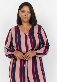 Blouse rayée multicolore présentant des nuances de rose, marine et bourgogne, avec un col en V, des manches bouffantes et des poignets élastiques.