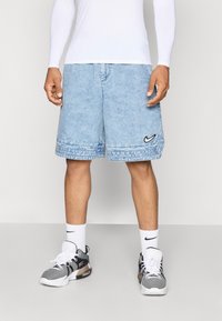 Lyseblå denimshorts med løs pasform, prydet med et sort Nike-logo, og parret med sort-hvide sportssko og hvide sokker.