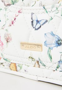 Sac à main synthétique blanc matelassé avec un motif floral mettant en vedette des papillons bleus. Accent en métal doré avec le logo ALDO sur le devant.