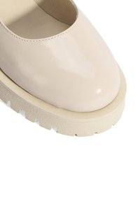 Beige lakleren schoen met een ronde neus en een chunky, gestructureerde zool. Heeft een minimalistisch ontwerp en een gladde, glanzende afwerking.