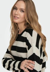 Maglione a righe nero e crema con un design a maglia larga, scollo rotondo e maniche lunghe. Presenta ampie righe orizzontali e polsini a costine.