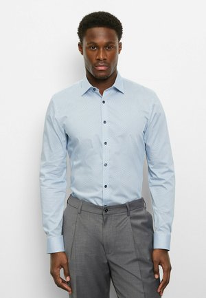 Hellblaues Hemd mit Knopfleiste, kleinem geometrischem Muster, langen Ärmeln und dunkelblauen Knöpfen, kombiniert mit grauer Anzughose.