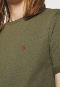 T-shirt verde oliva in cotone con collo a giro, maniche corte e un piccolo accento ricamato di colore rosso "II" sul lato sinistro del petto.