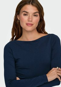 Granatowa bluzka z długim rękawem i okrągłym dekoltem, wykonana z miękkiego materiału, o dopasowanym kroju i gładkiej fakturze. Prosty i uniwersalny styl.
