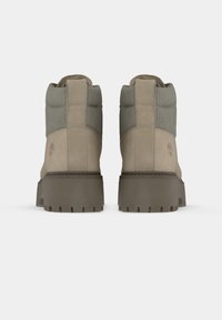 Beige ankelstøvler med teksturerte grå detaljer, robuste gummisåler og polstrede krager. Har Timberland-logo på siden.