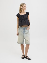 Čierny krátky top s volánovým výstrihom, skombinovaný s džínsovými bermudami v svetlom prání. Čierne ploché topánky dotvárajú outfit.