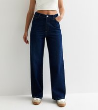 Wijdvallende donkerblauwe denim jeans met een hoge taille, voorzien van een voorvak en gestikte naden; gecombineerd met witte en beige sneakers.