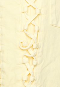 Tecido de denim amarelo claro com um detalhe de renda em cruz ao longo do lado. Apresenta uma textura suave e um pequeno bolso no canto superior direito.