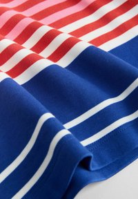 Bombažna srajca s horizontalnimi črtami v rdeči, rožnati, beli in modri barvi. Gladek tekstura, zavit rob in vidni šivi ob robovih.