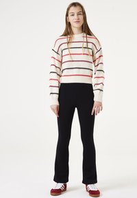 Suéter corto a rayas en crema, rojo y negro. Combinado con leggings acampanados negros y zapatillas rojas. Textura suave con acentos de canalé.
