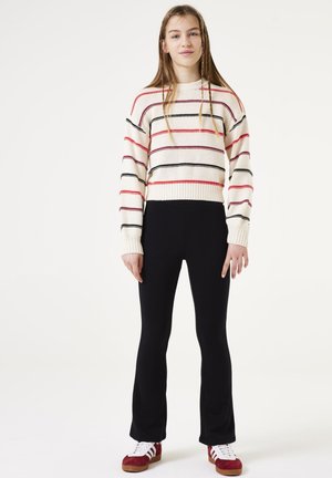 Pull cropped rayé en crème, rouge et noir. Associé à des leggings noirs évasés et des baskets rouges. Texture lisse avec des accents côtelés.