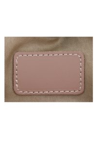 Brun tygbakgrund med en rektangulär rosa läderlappar, kantad med krämfärgad sömnad, med en slät yta.