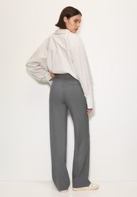 Lagano prugasta bijela i siva oversized košulja, sive široke hlače i bež tenisice. Glatki materijal s opuštenim krojem i dugim rukavima.