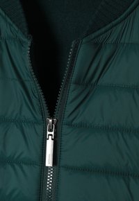 Dark green puffer jacket with a zippered front, featuring a ribbed knit collar and quilted texture. The zipper hardware is silver.